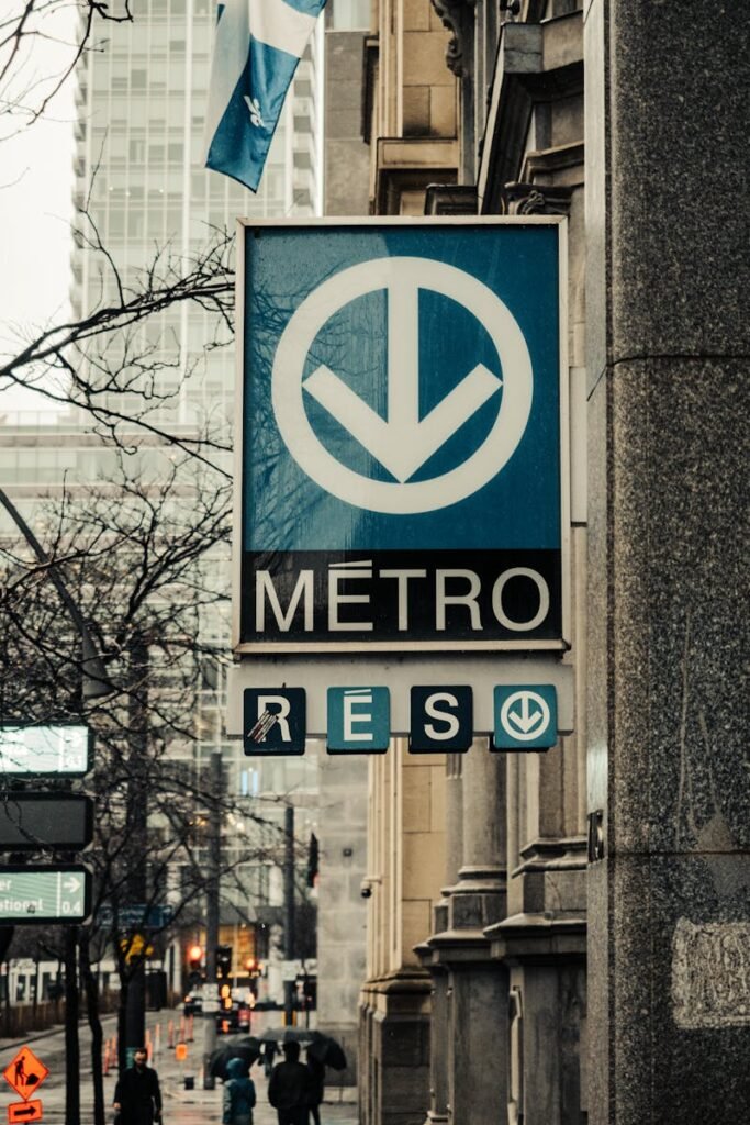 A street view of a Montreal Metro sign with city buildings and pedestrians in the background.